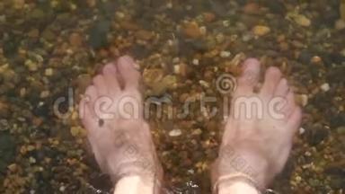 一个人光着脚在海里的鹅卵石海滩上，水冲走了一个人的脚